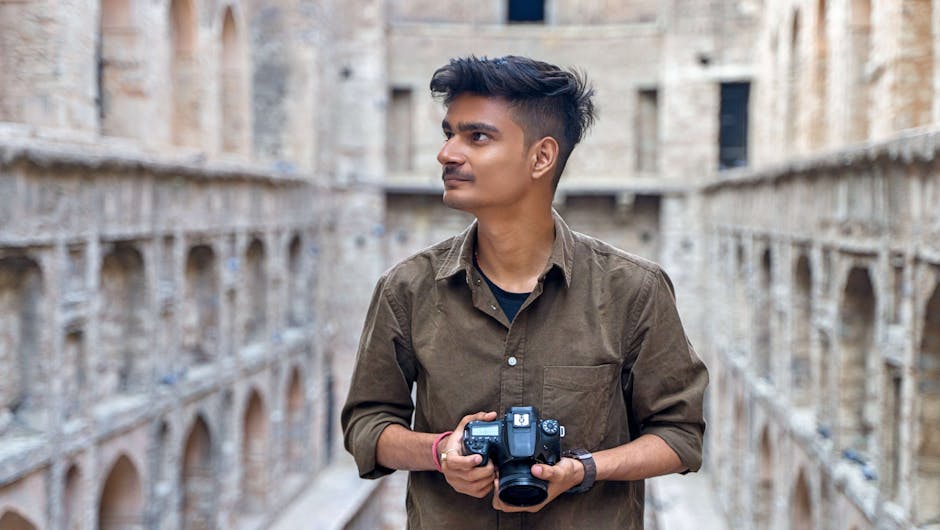 A young man holding a camera in a historic architectural setting outdoors.