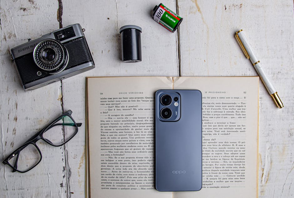 A flat lay of a vintage camera, smartphone, and accessories on an open book.