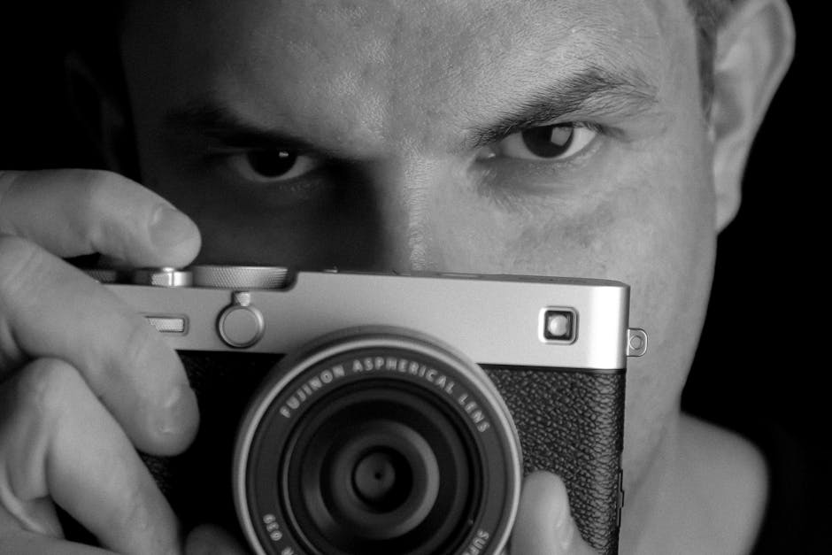Black and white portrait of a photographer holding a camera, focus on the face.